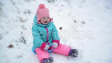 穿着温暖的雪服和粉红色针织帽的幼儿女孩坐在Saucer雪橇上。 可爱的儿童享受冬季户外活动